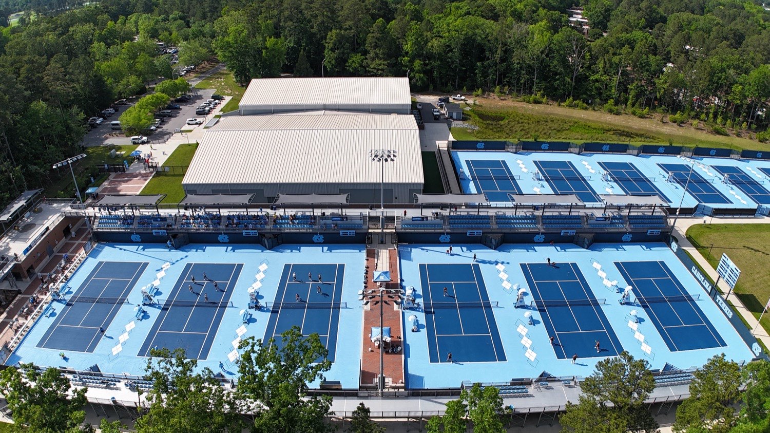 Aerial view of the Chewning Tennis Center at UNC Chapel Hill, showing the full spread of Carolina blue outdoor courts alongside the indoor facility.
